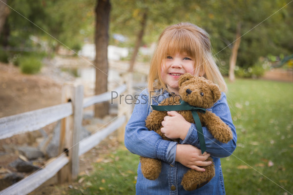 Cute Smiling Young Girl Hugging Her Teddy Bear on Bench Outside.