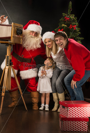Santa Claus taking picture of full family with old wooden camera at home near Christmas tree. Capturing moments of happiness