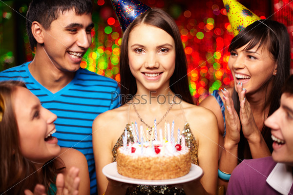 Portrait of joyful girl with birthday cake surrounded by friends at party
