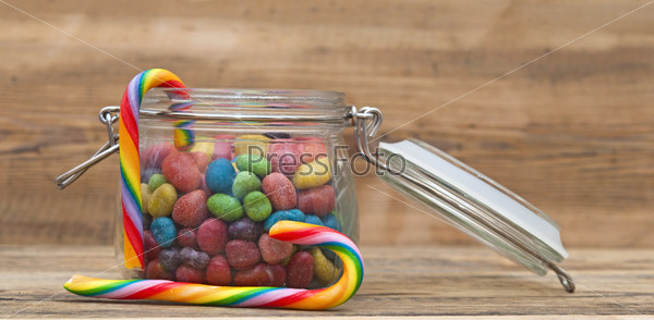 Sweet sugar candies in glass jars on wooden background