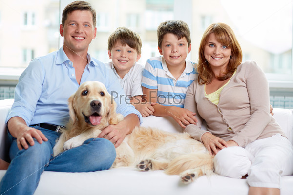 Cheerful Family With Their Pet Sitting On Sofa At Home