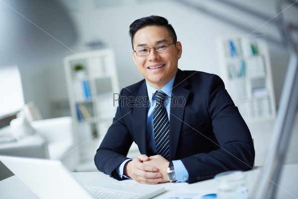 Smiling businessman in suit looking at camera in office, stock photo