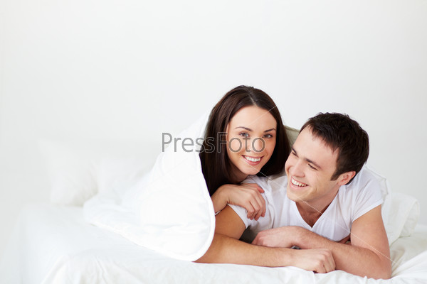 Portrait of joyful young couple lying in bed and laughing