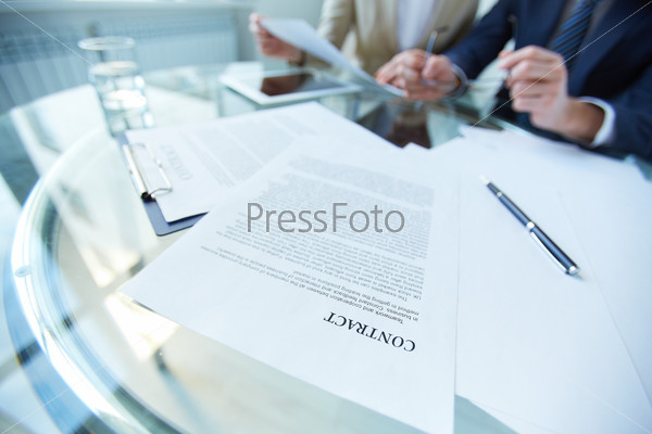 Business documents and pen at workplace with working people on background