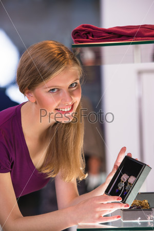 Young woman looking at the shop showcase and taking earrings to look at it closer