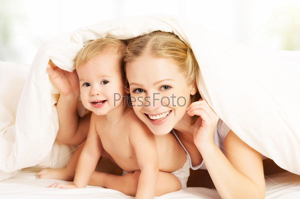 Happy family mother and baby under blankets in bed
