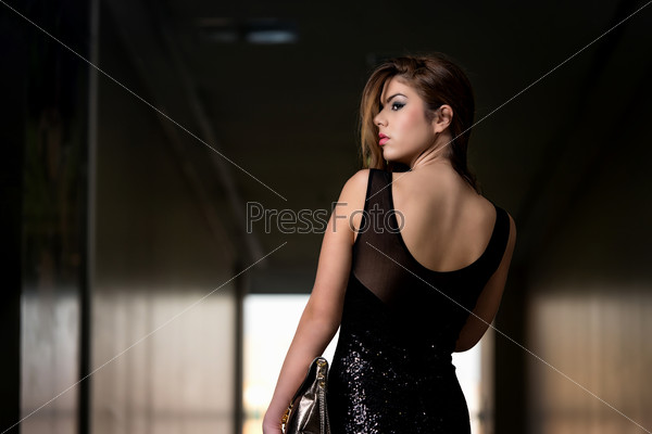 Fashion Model From Behind In Beautiful Black Dress . Portrait Of Young And Beautiful Fashion Model In The Shopping Mall . Professional Makeup And Hair Style