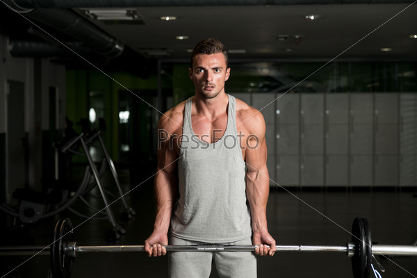 Young Men Doing Heavy Barbell Exercise. Young Athlete In The Gym Performing Biceps Curls With A Barbell