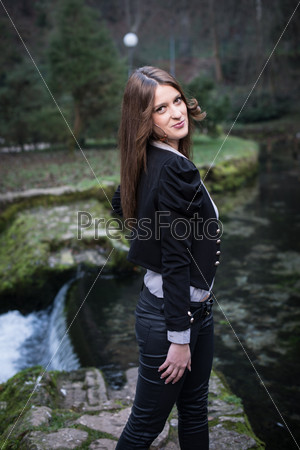 Young woman in jacket looking behind her shoulder and smiling at the lake, stock photo