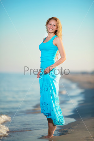 Young smiling blond woman in blue t-shirt and skirt posing near the sea