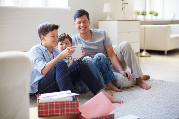 Portrait of cute boy opening envelope with his father and brother near by at home