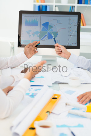 Image of human hands pointing at computer screen in working environment at meeting