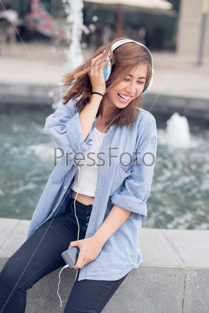 Vertical image of a cheerful young girl listening to the music with her earphones outside