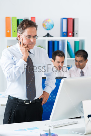 Vertical image of a businessman contemplating standing in front of the computer monitor on the foreground