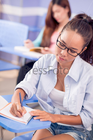 Vertical image of a serious student taking notes in lecture in the college