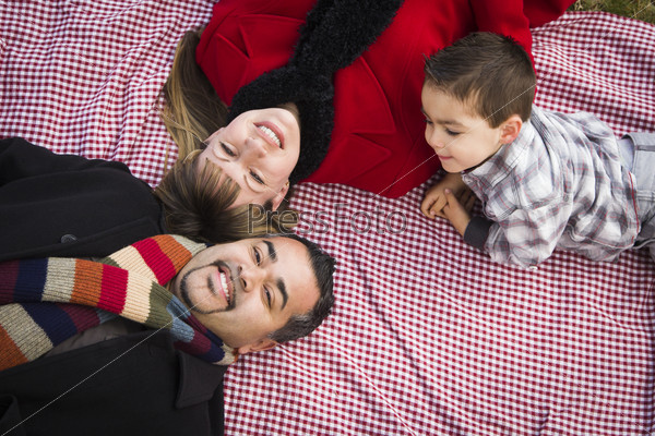 Young Mixed Race Family in Winter Clothing Laying on Their Backs on Picnic Blanket in the Park Together.