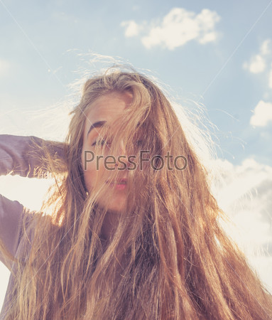 Girls face half hide by her long blond hair. Portrait of happy woman smiling against clear sky