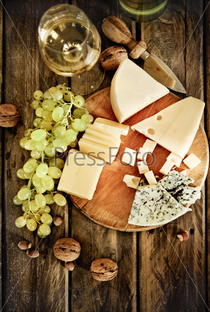 Bottles and glass of white wine, cheese, nuts and grapes on wooden background
