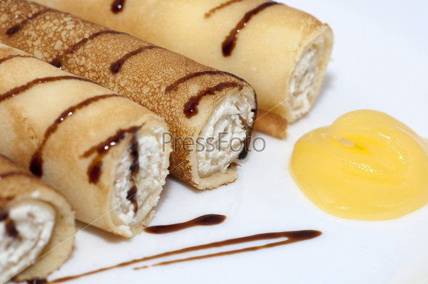 Pancake rolls with sweet cottage cheese served with honey on white plate