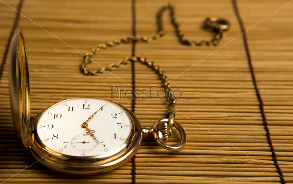 Gold pocket watch on bamboo rugs close-up