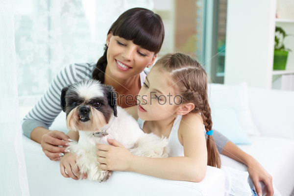 Portrait of happy girl holding pet and looking at it with her mother near by