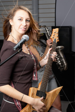Young woman with rock guitar at music equipment background