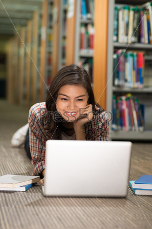 Student lying on floor with laptop in library