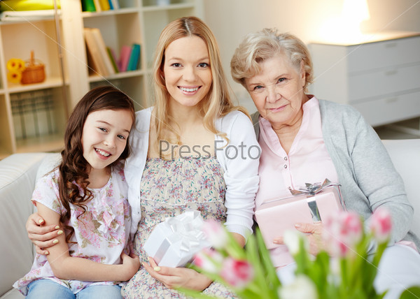 Portrait of happy little girl, her mother and grandmother with giftboxes looking at camera at home