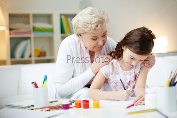 Portrait of cute girl making card for her mom with her grandmother near by