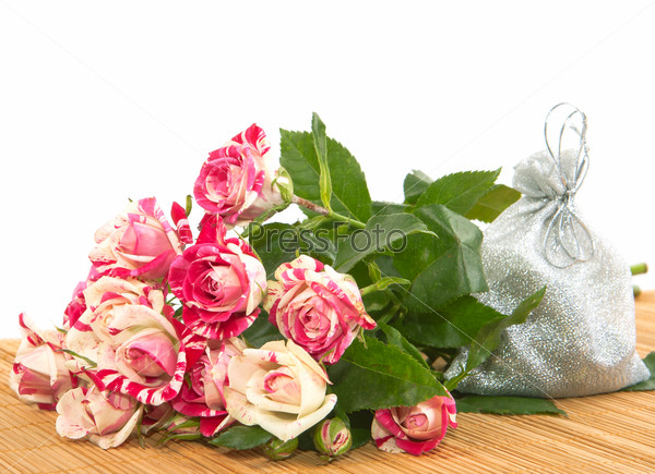 Beautiful roses and a small bag with a gift on a substrate of bamboo sticks.