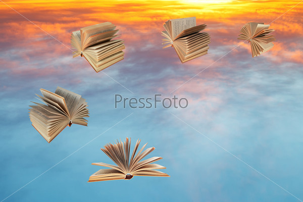 books fly over sunset clouds
