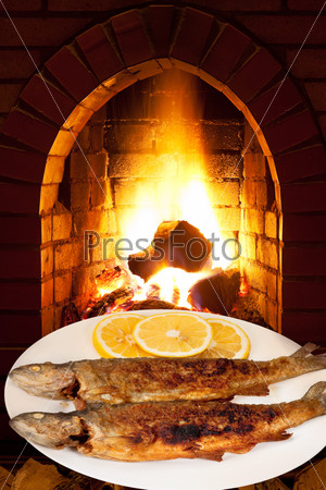 fried trout fish on white plate and open fire in wood burning oven