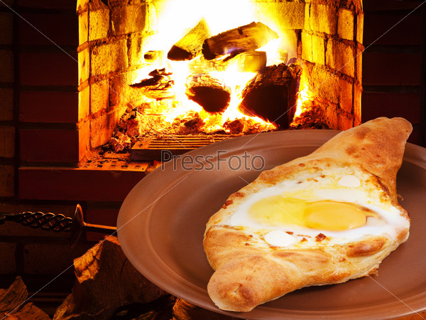 adzharia hachapuri with egg on plate and open fire in wood burning stove