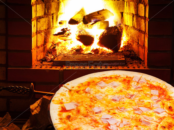 Italian pizza with prosciutto cotto and open fire in wood burning oven, stock photo