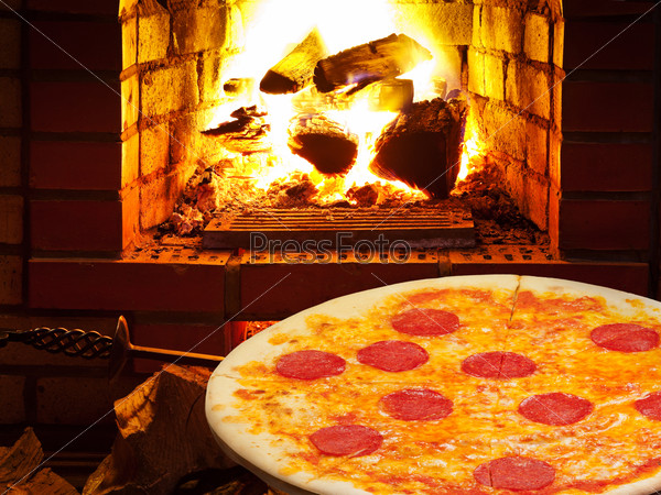 Italian pizza with salami and open fire in wood burning oven, stock photo