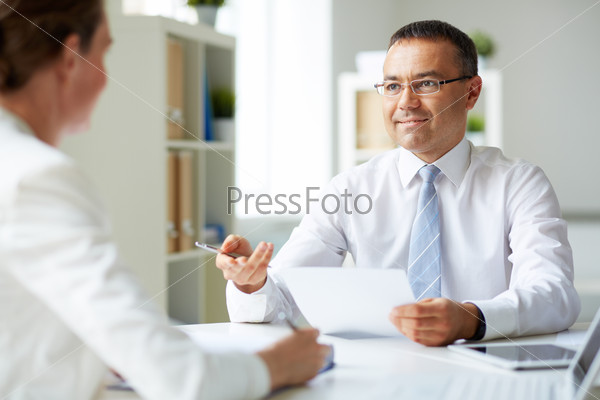 Portrait of mature businessman looking at his secretary while speaking to her