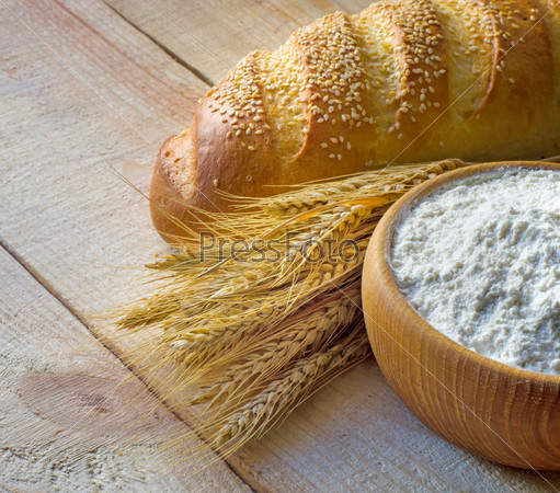 Wooden bowl full flour , bread and wheat ears on wooden background