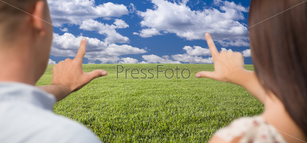 Couple Framing Hands Around Space in Grass Field and Sky on the Horizon.