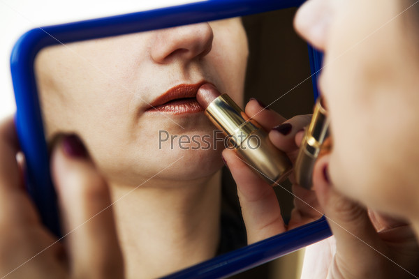woman paints lips with lipstick before a mirror closeup