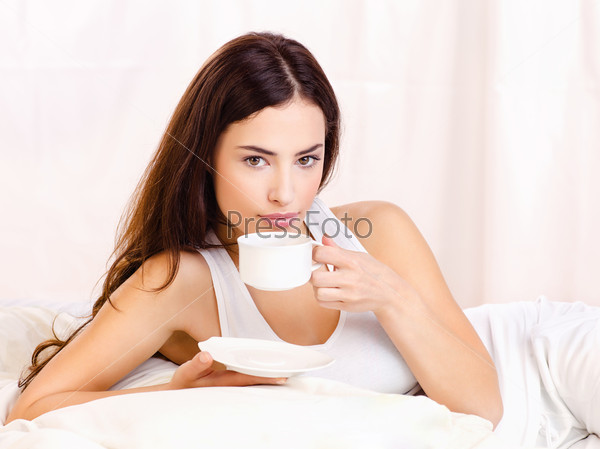 Woman holding cup of coffee in bed