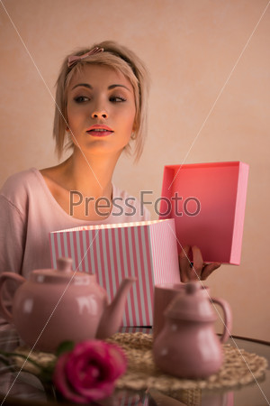 Young beautiful woman opening gift box while having tea-party. She is very satisfied. Valentine\'s day or international women\'s day celebration.