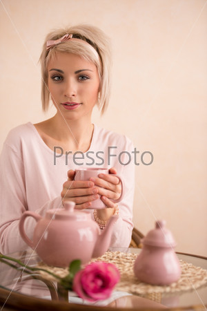 Young beautiful woman having tea-party in pink feminine style. She is very satisfied. Valentine\'s day or international women\'s day celebration.