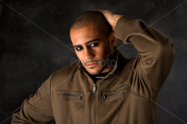 Handsome African Hispanic guy frowning with strong macho expression and dark eyes in green vest and hand on head