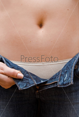 Young woman opening her blue jeans showing a rim of her white underwear and bare belly up to her bellybutton