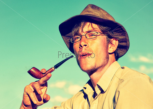 Colorized vintage outdoor portrait of man in hat is smoking tobacco-pipe