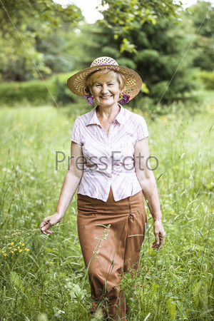 Serenity. Friendly Senior Peasant Woman in Straw in Meadow Smiling