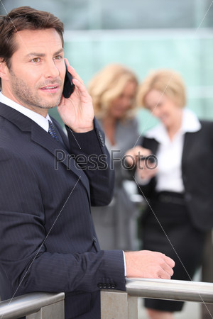 Businessman holding mobile telephone with colleagues in background