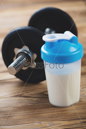 Protein shake with a dumbbell in the background, vertical shot