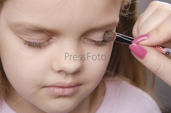 Makeup artist in the process of makeup colors eyelids on the face five year old girl