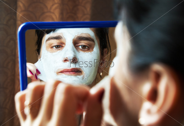 young beautiful woman takes beauty mask in front of mirror